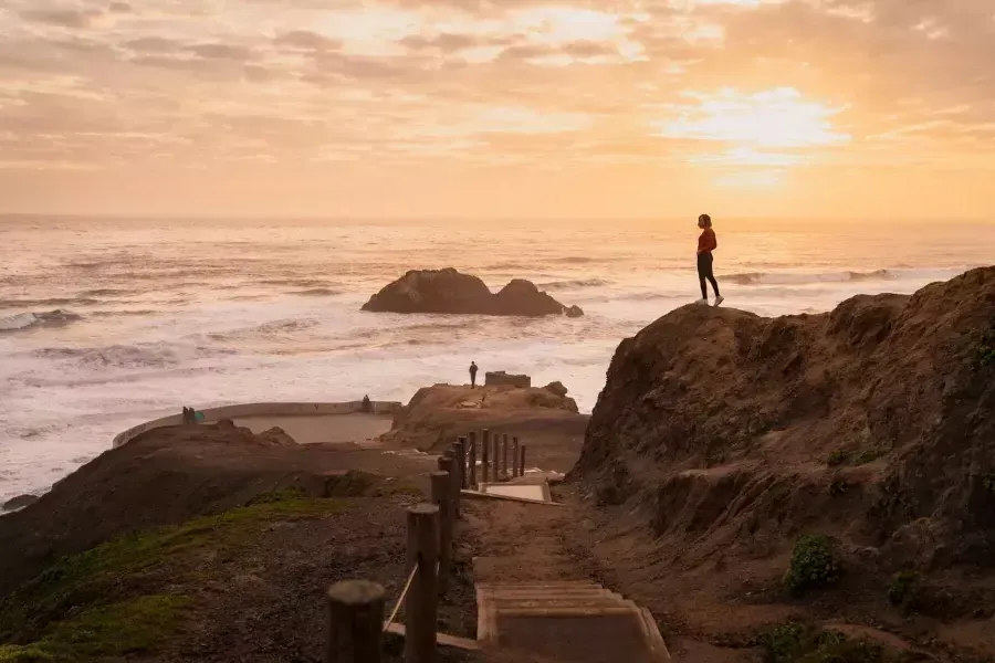 Due persone stanno sulle rocce che si affacciano sull'oceano ai Sutro Baths di 贝博体彩app.