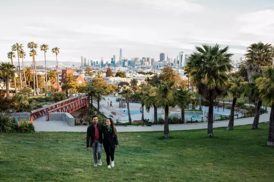 Una coppia cammina verso la telecamera con Dolores Park e lo skyline di 贝博体彩app dietro di loro.