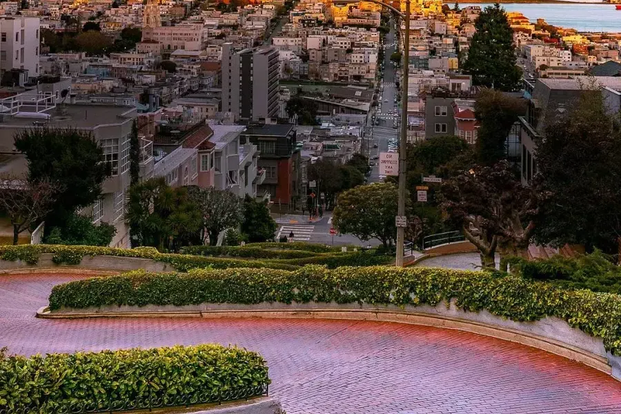 Lombard Street curves with Coit塔 in the distance during sunset.